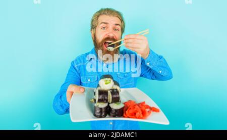 Bearded man eating sushi with chopsticks. Japanese food delivery. Pickled ginger and sushi on plate. Stock Photo