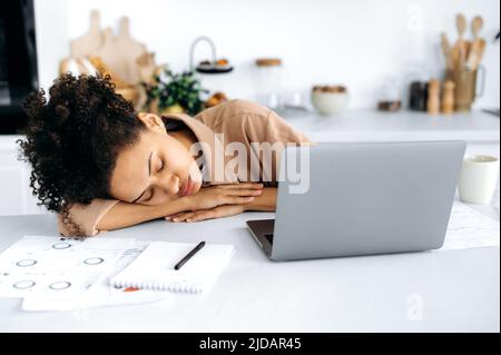 Chronic sleep deprivation. Exhausted african american girl, female freelancer or student, fell asleep at the desktop near the laptop, overworked from working or studying online, needs rest and sleep Stock Photo