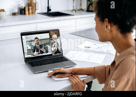 Over shoulder view of African American girl of laptop screen with multiracial people. Female brainstorming with work colleagues, listening to online webinar using laptop and video conference Stock Photo