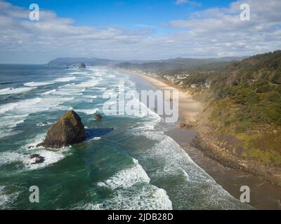 Sea coast. Turquoise water of the ocean with light white waves, a large boulder in the water, a green hilly coast. A mountain range is visible on the Stock Photo