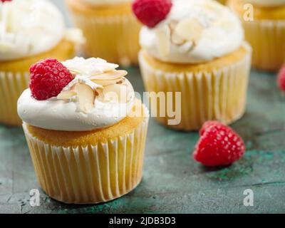 Festive sweet dessert - muffins with cream, raspberries and almonds on a dark green background. Food background. Holiday, banquet, birthday, picnic. R Stock Photo