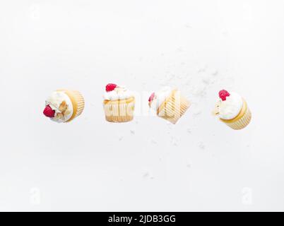 Small muffins with cream and fresh berries on a white background in a frozen flight. Minimalism. There are no people in the photo. There is free space Stock Photo