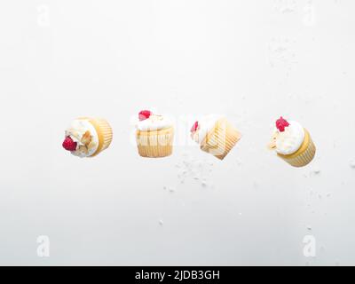 Light sweet dessert - small muffins with cream and fresh raspberries. Isolated on white background. Levitation. Sweet food, calories. Holiday, birthda Stock Photo