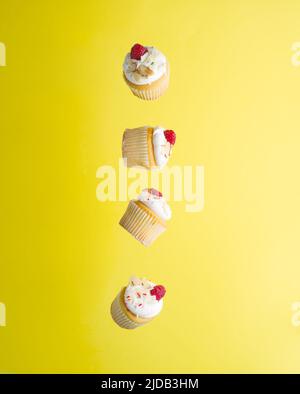 Creative composition. Small appetizing muffins with whipped cream and raspberries in a frozen flight on a bright yellow background. Holiday, birthday, Stock Photo