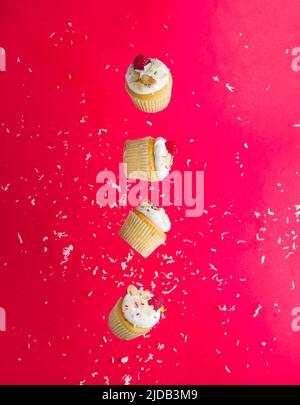 On a bright pink background with white confetti, small muffins with cream and fresh raspberries in a frozen flight. Creative holiday composition. Mini Stock Photo