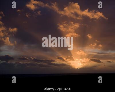 Sunset at sea with partly cloudy sky and sun rays; Brighton, East Sussex, England Stock Photo
