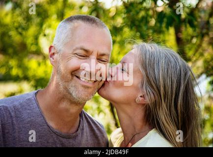 Portrait of a mature couple together outside with woman kissing her husband's cheek; Edmonton, Alberta, Canada Stock Photo