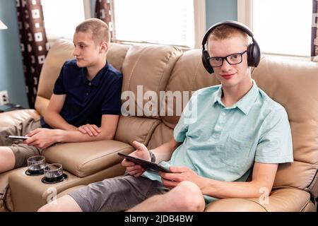 Young adult brothers using tablet and smart phone together at home; Edmonton, Alberta, Canada Stock Photo