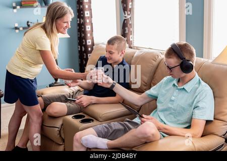 Mother serving drinks to young adult sons using technology at home; Edmonton, Alberta, Canada Stock Photo