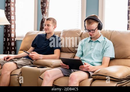 Young adult brothers using tablet and smart phone together at home; Edmonton, Alberta, Canada Stock Photo