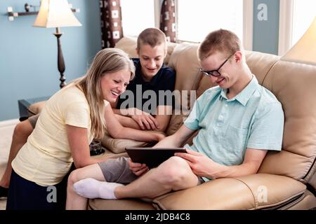 Mother and young adult brothers using tablet together at home; Edmonton, Alberta, Canada Stock Photo
