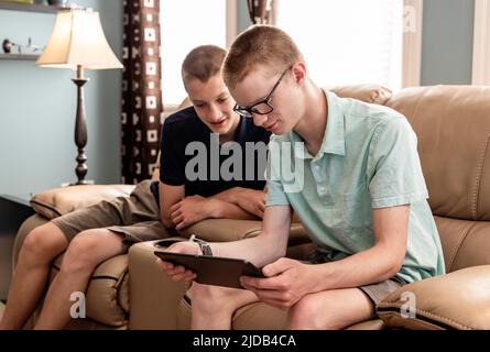 Young adult brothers using tablet and smart phone together at home; Edmonton, Alberta, Canada Stock Photo