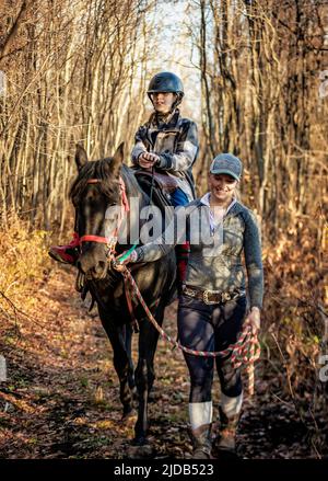 A young girl with Cerebral Palsy and her trainer working with a horse on a trail ride during a Hippotherapy session; Westlock, Alberta, Canada Stock Photo