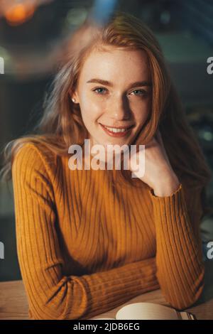 Portrait of a caucasian woman student with a book smiling at camera enjoying learning pastime at home. Happy redhead lady posing with educational Stock Photo