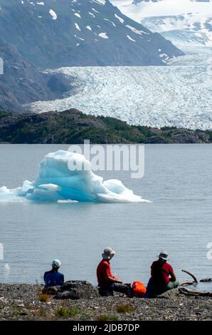 Hikers take a break to watch icebergs push against the shore of the lake at Grewingk Glacier in Kachemak Bay State Park, across from Homer, Alaska Stock Photo