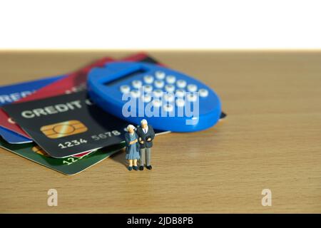 Miniature people toys conceptual photography. Elderly couple standing above credit card, paying, and buying household stuff. Image photo Stock Photo