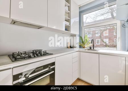 Light small home kitchen with wide window furnished with cupboards and shelves with appliances in modern urban apartment Stock Photo