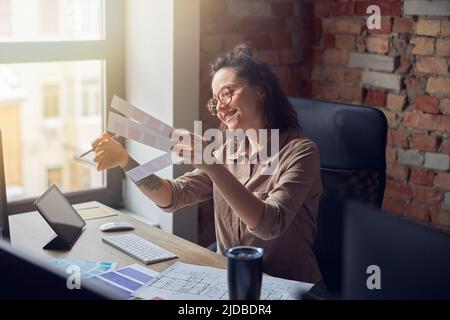 Creative female interior architect or designer looking at color samples while working on a project, sitting at the desk in her office Stock Photo