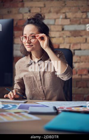 Concentrated female interior architect or designer working on a project, using computer, selecting color samples while sitting at the desk in her Stock Photo