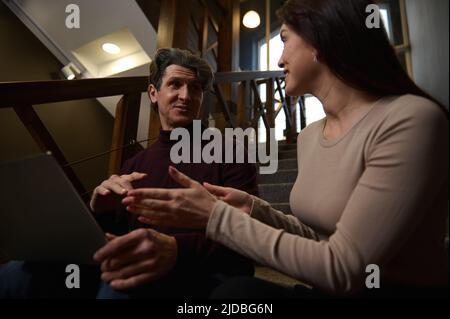 They are great team together. Friendly colleagues, business partners planning new projects sitting close to each other on stairs in a modern office li Stock Photo