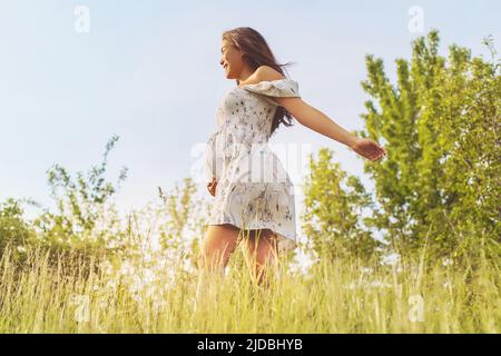 Natural pregnancy healthy Asian pregnant woman walking in nature fields for eco-friendly sustainability baby bump concept. Girl in feminine dress with Stock Photo
