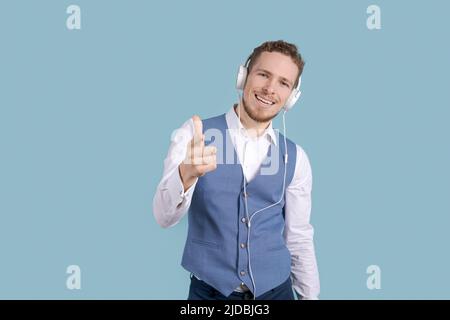 Technology, gadgets and people. Carefree business man listening to his favorite song in headphones, using a mobile phone, singing and dancing on a blue background Stock Photo