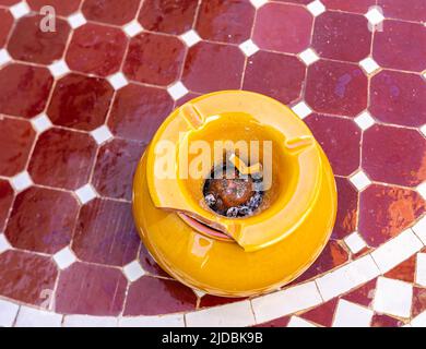 Yellow Arabic ashtray on dark red table - Moroccan home features Stock Photo