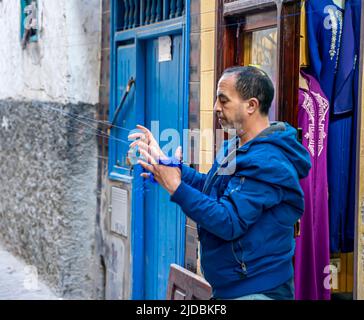 A man working on knitting threads - knitting material for professional clothing production in front of his clothes store. Essaouira. Morocco Stock Photo