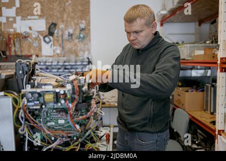 Repairman with screwdriver fixing coffee machine at table indoors Stock Photo