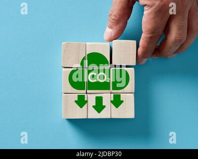 Male hand arranging wooden cubes with CO2 emission reduction icon. Zero carbon dioxide emission, renewable energy, low pollution, environmental protec Stock Photo