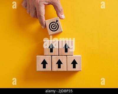 Hand placing a target over the wooden cubes with arrow icons. Achieving business objectives, goal setting and business development concepts. Stock Photo