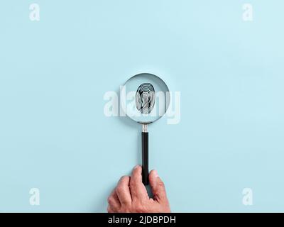 Male hand holds a magnifying glass or magnifier focusing on a fingerprint. Forensic identification concept. Stock Photo