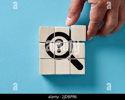 Male hand arranging wooden cubes with a magnifier and question mark icon. Problem solving, analysis, research or discovery concepts. Stock Photo