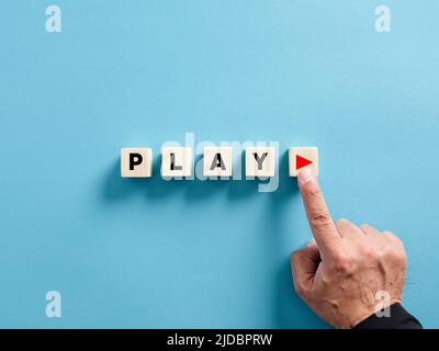 Male hand presses the play button with the word play on wooden cubes. Stock Photo