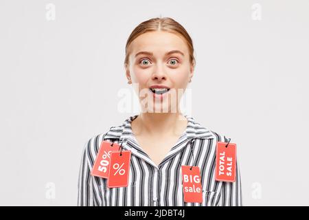 Cheerful shocked young woman with sale tags on blouse keeping mouth open and looking at camera Stock Photo