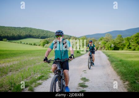 Active senior couple riding electric bicycles on trail at summer park, healthy lifestyle concept. Stock Photo