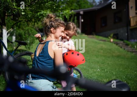 Young mother with little daughter preaparing for bike ride, putting on helmets. Stock Photo