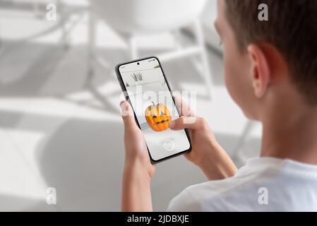 Boy on a mobile phone is playing an augmented reality game. View over shoulder at the phone display. Pumpkin throwing game concept Stock Photo