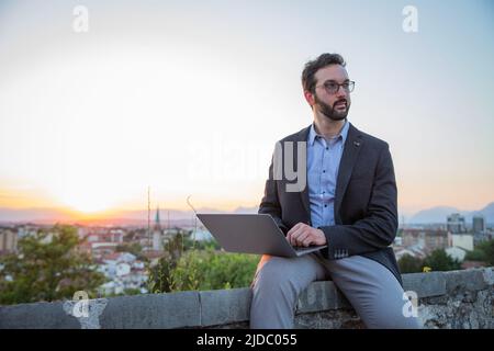 Elegantly dressed businessman uses his laptop outside with sunset Stock Photo