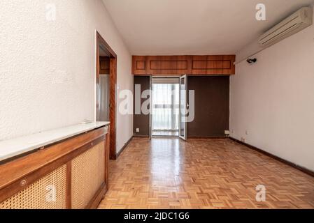 Empty living room with oak parquet floors, wooden radiator cover and white and brown painted walls Stock Photo