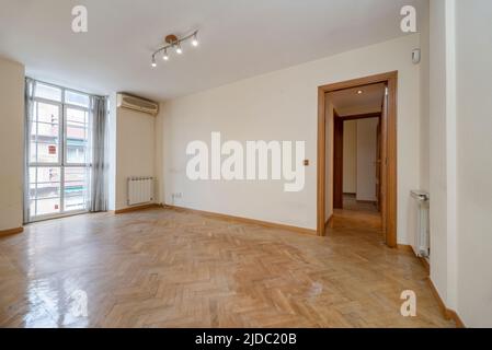 Empty room with light oak parquet, balcony with aluminum windows and radiator next to the window and white painted walls with oak carpentry Stock Photo