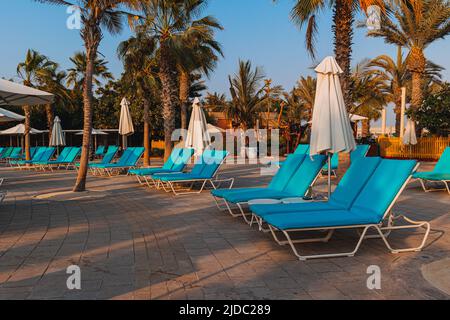 Blue bed pool with a towel stand under umbrellas against the backdrop of beautiful palm trees, rest, vacations, relaxation. Stock Photo