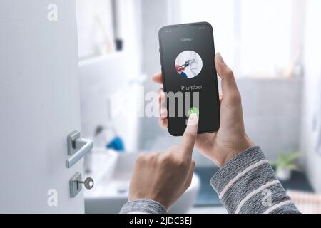 Woman calling a plumber on her smartphone, she has a water leak in the bathroom Stock Photo
