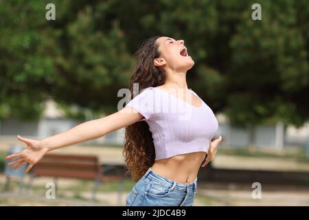 Excited woman outstretching arms shouting to the air in a park Stock Photo