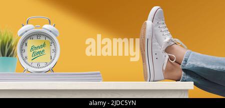 Woman with feet up on a desk and alarm clock with sticky note, it's break time Stock Photo