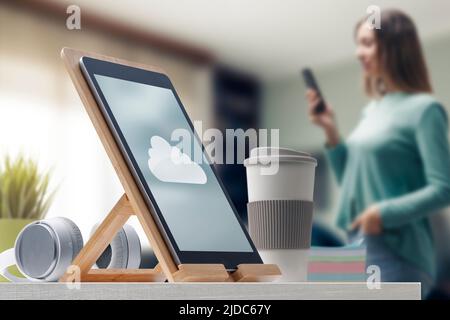 Cloud computing service app on digital tablet and woman using a smartphone in the background Stock Photo