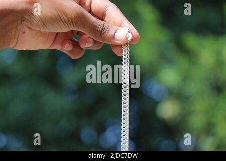 The silver chain held in hand on natural green background Stock Photo