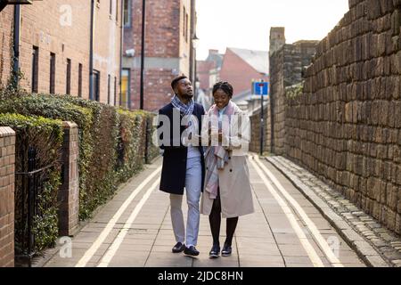 Couple walking along back lane alongside old stone wall, woman holding cell phone Stock Photo