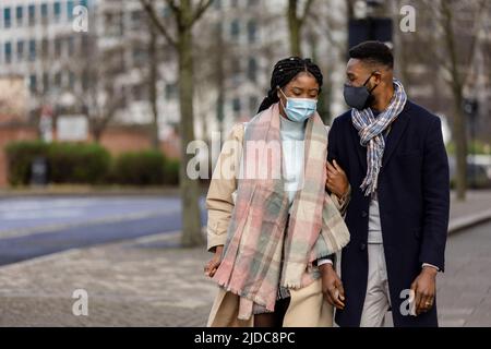 Couple with face coveings walking arm in arm in city cente Stock Photo