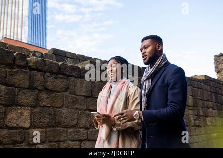 Woman smiling and holding mobile phone walking alongside man who is talking Stock Photo